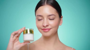 Güzellik kraliçesi yüzüne krem sürüyor. Temiz tenli genç bir kadın. Yüz kremi kavanozu olan bir model.