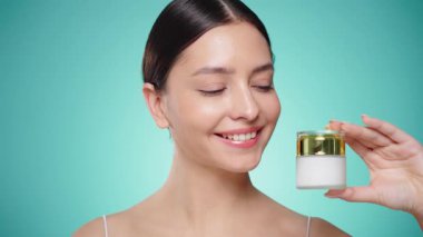 Güzellik kraliçesi yüzüne krem sürüyor. Temiz tenli genç bir kadın. Yüz kremi kavanozu olan bir model.