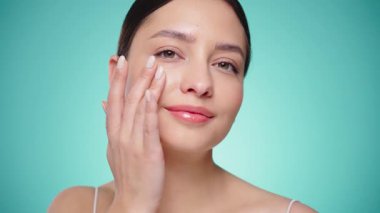 Güzel Genç Kadın Kusursuz Yüzüne Dokunuyor. Doğal Kozmetik Teni Ürünleri. Kadın nemlendirici yüz bakımı gösteriyor. İzole edilmiş arkaplanı olan yakın plan portresi yükseliyor. Yavaş çekim