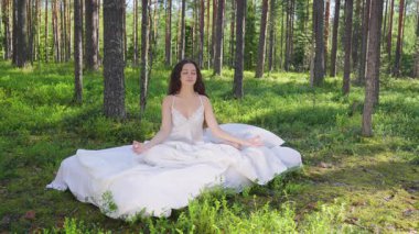 Yaz ormanında yatakta dinlenen genç bir kadın. Kız ormanda nilüfer çiçeği pozisyonunda meditasyon yapıyor. Yavaş çekim videosu