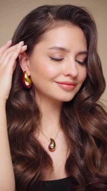 Güzel model kadınların dalgaları ve parlak saçları vardır. Kıvırcık saçlı, küpeli ve mücevherli esmer kız. Yavaş çekim videosu