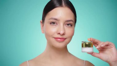 Güzellik kraliçesi yüzüne krem sürüyor. Temiz tenli genç bir kadın. Yüz kremi kavanozu olan bir model.