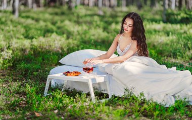 Kadın bir yaz ormanında uyanıyor. Genç bir kadın yaz ormanında yatakta kahvaltı yapıyor.