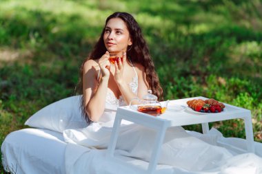 Kadın bir yaz ormanında uyanıyor. Genç bir kadın yaz ormanında yatakta kahvaltı yapıyor.