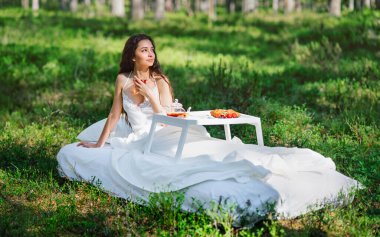 Kadın bir yaz ormanında uyanıyor. Genç bir kadın yaz ormanında yatakta kahvaltı yapıyor.