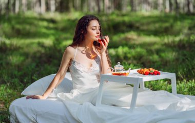 Kadın bir yaz ormanında uyanıyor. Genç bir kadın yaz ormanında yatakta kahvaltı yapıyor.
