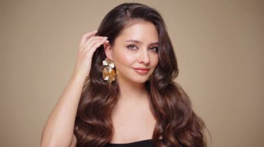 Güzel model kadınların dalgaları ve parlak saçları vardır. Kıvırcık saçlı, küpeli ve mücevherli esmer kız. Yavaş çekim videosu