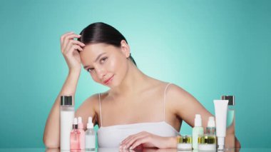 Doğal malzemelere dayalı kozmetik ürünler, fırça, tonik, vücut bakımı. Doğal kozmetik ürünleri. Açık mavi arka planda, kozmetik işlemleri için kavanozlar, şişeler ve tüplerin arasında genç bir kadın.