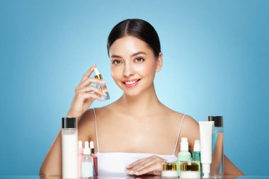 Doğal malzemelere dayalı kozmetik ürünler, fırça, tonik, vücut bakımı. Doğal kozmetik ürünleri. Açık mavi arka planda, kozmetik işlemleri için kavanozlar, şişeler ve tüplerin arasında genç bir kadın.