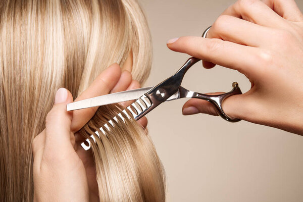 Парикмахер стрижет длинные светлые волосы ножницами. Парикмахерская, парикмахер. Уход и косметика для волос. Красные волосы
