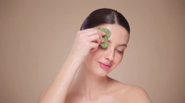 Cilt bakımı rutini yapan güzel genç bir kadın, hurda, yüz masajı, yeşim taşıyla yüz bakımı, yaşlanma ve kozmetik temizleme için yüz bakımı. Yavaş çekim