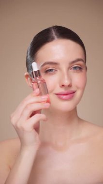 Elinde kozmetik yağ serumu ya da hyaluronik asit dolu bir kavanoz tutan güzel genç kadın. Mükemmel bir yüz derisi. Kozmetik cilt bakımı. Yavaş çekim, dikey video