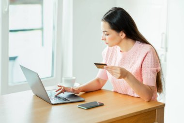 Genç, çekici bir kadın, kredi kartıyla dizüstü bilgisayarla online alışveriş yapıyor. E-ticaret, iş konsepti. Serbest, uzak çalışma