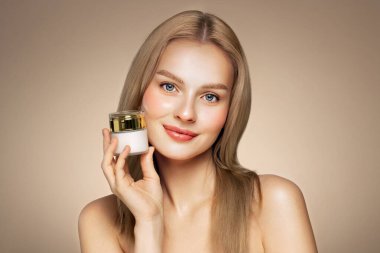 Güzel sarışın kadın yüzüne krem sürüyor. Temiz tenli genç bir kadın. Yüz kremi kavanozu olan bir model.