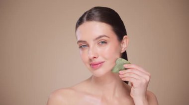 Cilt bakımı rutini yapan güzel genç bir kadın, hurda, yüz masajı, yeşim taşıyla yüz bakımı, yaşlanma ve kozmetik temizleme için yüz bakımı. Yavaş çekim