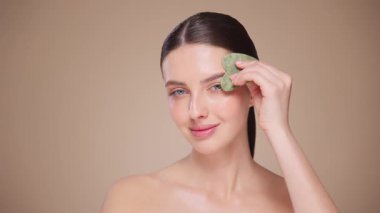 Cilt bakımı rutini yapan güzel genç bir kadın, hurda, yüz masajı, yeşim taşıyla yüz bakımı, yaşlanma ve kozmetik temizleme için yüz bakımı. Yavaş çekim