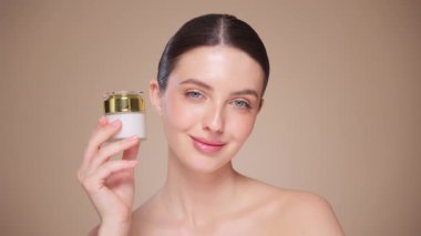Güzellik kraliçesi yüzüne krem sürüyor. Temiz tenli genç bir kadın. Yüz kremi kavanozu olan bir model.