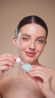 Elinde kozmetik yağ serumu ya da hyaluronik asit dolu bir kavanoz tutan güzel genç kadın. Mükemmel bir yüz derisi. Kozmetik cilt bakımı. Yavaş çekim, dikey video