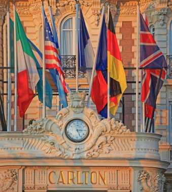 Cannes, France - January 20, 2012: International Flags and IWC Clock at Luxury Carlton Five Star Hotel Sunny Winter Day French Riviera. clipart