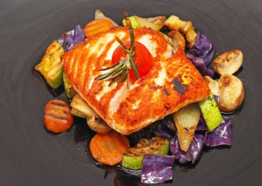 Siyah tabakta servis edilen sebzeli ızgara somon filetosu.