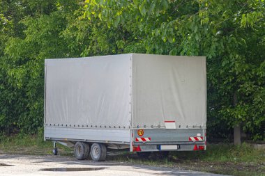 Park yerinde gri plastik paraşüt örtüsü olan küçük tekerlekler çift akslı römork.
