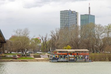 Belgrade, Serbia - March 11, 2024: Skyscraper Microsoft Office Building Usce Twin Towers and Floating Zappa Barka Floating Club Barge at Sava River Winter Day. clipart