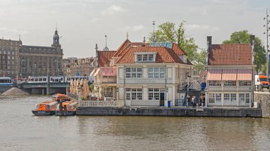 Amsterdam, Netherlands - May 16, 2018: Lovers Canal Cruises Sightseeing Excursions Boat Tour Agency and Cafe Restaurant Loetje Building at Stationsplein Spring Day. clipart