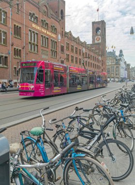 Amsterdam, Hollanda - 16 Mayıs 2018: Şehir merkezinde Damrak Caddesi 'ndeki Van Berlage Binası ve Bisiklet Otoparkı' nda toplu taşıma tramvayı.