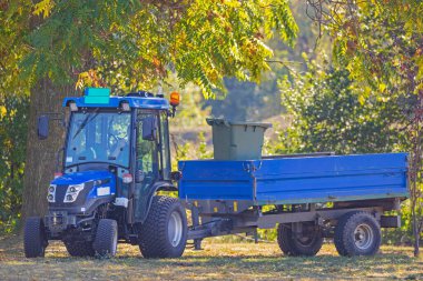 Şehir parkında mavi römorklu küçük traktör.