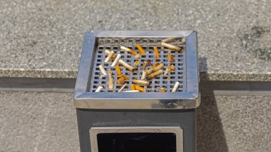 Güneşli bir günde sigara izmaritleri kare şeklinde metal kül tablasında