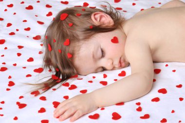 Beyaz kalple çevrili kırmızı kalplerle uyuyan bir bebek..