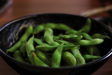 A black bowl filled with salted edamame. clipart
