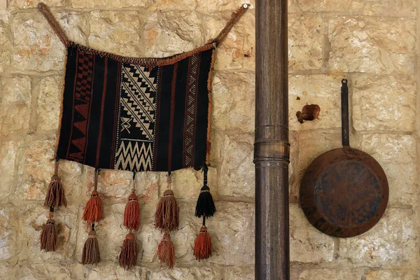 Decorative rug and pan on an indoor stone wall,