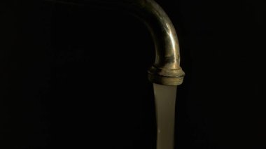 Kirli su, karanlıkta kirli bir musluktan akıyor, siyah bir arka planda.