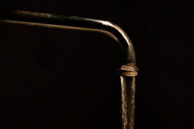 Karanlıktaki kirli bir musluktan akan su, siyah bir arka planda.