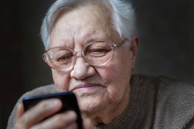 Gözlüklü büyükanne gülümsüyor, akıllı telefona bakıyor, yakın plan.