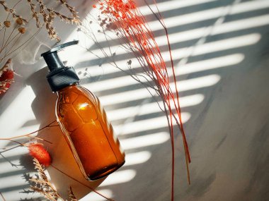 Kehribar cam şişedeki kozmetik sıvı maddeyi ve beyaz mermer arka plandaki kuru çiçek dallarını kapatın. Cilt ve vücut bakımı için güzellik ürünleri. Banner Arkaplan. Kozmetik kavramı.