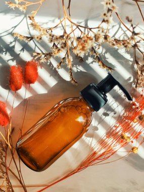 Kehribar cam şişedeki kozmetik sıvı maddeyi ve beyaz mermer arka plandaki kuru çiçek dallarını kapatın. Cilt ve vücut bakımı için güzellik ürünleri. Banner Arkaplan. Kozmetik kavramı.