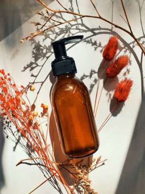 Kehribar cam şişedeki kozmetik sıvı maddeyi ve beyaz mermer arka plandaki kuru çiçek dallarını kapatın. Cilt ve vücut bakımı için güzellik ürünleri. Banner Arkaplan. Kozmetik kavramı.