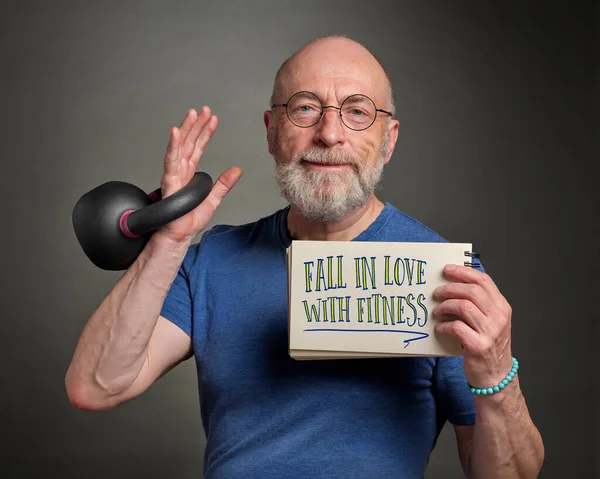 fall in love with fitness - senior man (in late 60s) with sketchbook sign is exercising with iron kettlebell, active senior and fitness concept
