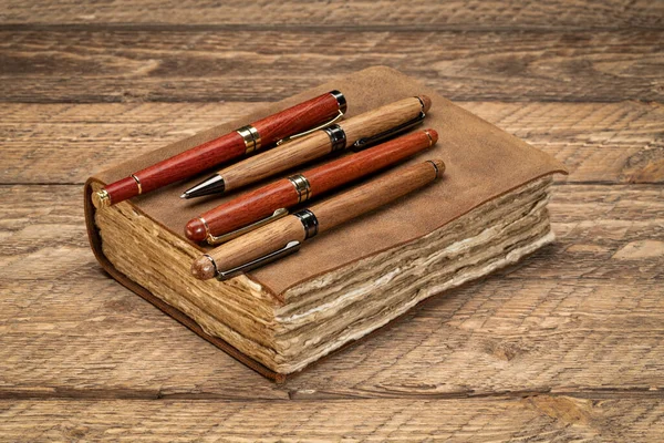 レトロな革を結んだジャーナルは 端の手作りの紙のページと素朴な木製のテーブルの上にスタイリッシュなペンのコレクション 執筆とジャーナリングのコンセプト — ストック写真