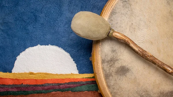 stock image handmade, native American style, shaman drum covered by a goat skin with a beater against abstract paper landscape with a rising moon