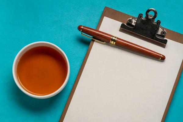 お茶とスタイリッシュなペンでお茶のカップとデスクトップフラットレイとクリップボード — ストック写真
