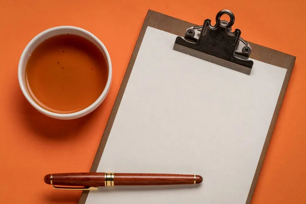 夹杂着空白纸片的剪贴板 桌上平铺着一杯茶和一支时髦的钢笔 — 图库照片