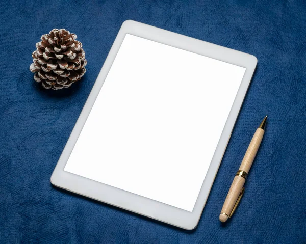 mockup of digital tablet with a blank isolated screen (clipping path included), flat lay with a frosty pine cone on blue textured paper