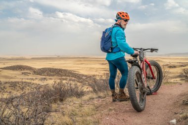 Kuzey Colorado otlağında tek bir patika üzerinde şişman bir dağ bisikleti olan yaşlı bir erkek bisikletçi. İlkbahar başlarında Fort Collins yakınlarındaki Soapstone bozkırında doğal manzara.