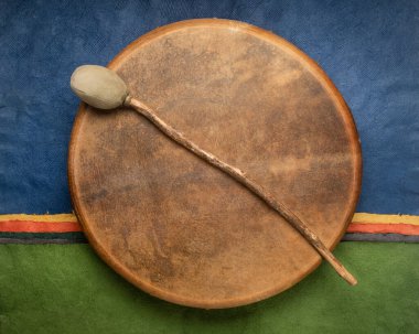 handmade, native American style, shaman frame drum covered by goat skin with a beater against colorful abstract paper landscape