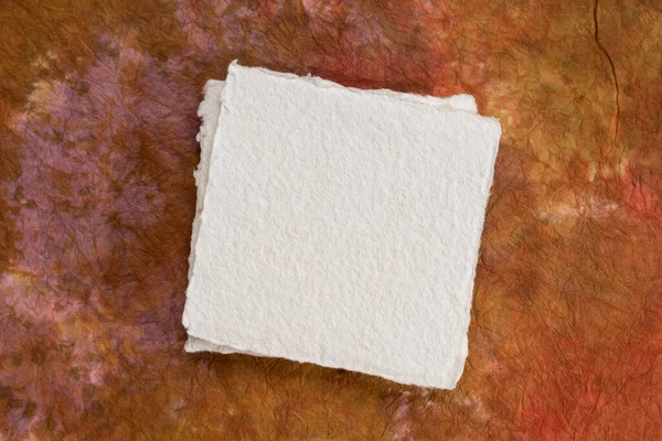 カラフルな大理石の紙に対する空白の白いKhadi紙の小さな正方形のシート — ストック写真