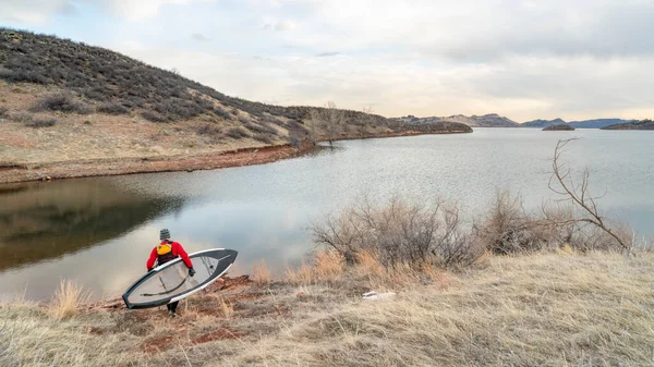 ドライスーツの男性パドラーとライフジャケットはコロラド州北部のホーストース貯水池の海岸に彼のパドルボードを運んでいます 冬のパドリングとトレーニングの概念 — ストック写真
