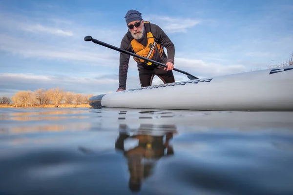 コロラド州の冬または早春の湖の上のシニアパドラーと彼のパドルボード カエルの視点 部分的に水中アクションカメラ — ストック写真